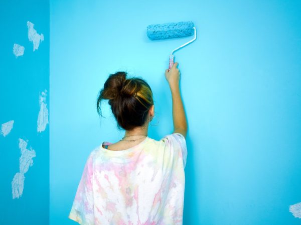 happy woman painting interior wall with paint roller in new house